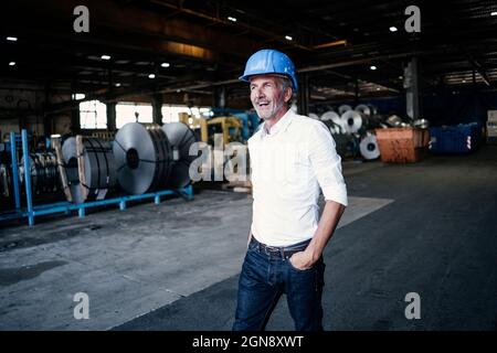 Cheerful male engineer with hand in pocket walking in steel mill Stock Photo