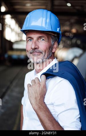 Male engineer with hardhat and blazer standing at warehouse Stock Photo