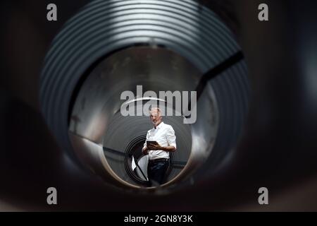 Businessman with digital tablet seen through rolled up metal sheet Stock Photo