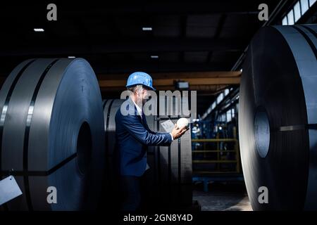 Businessman with hardhat holding globe while standing at steel industry