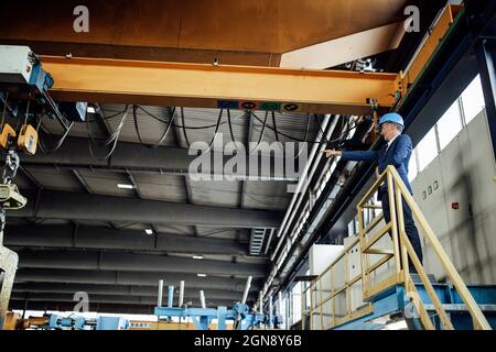 Male engineer pointing at overhead crane while standing in steel mill Stock Photo