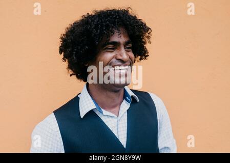 Cheerful man with curly black hair in front of beige wall Stock Photo