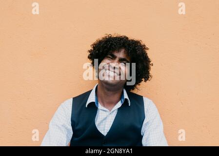 Cheerful man with curly black hair leaning on beige wall Stock Photo