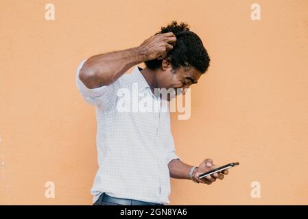 Frustrated man using smart phone in front of beige wall Stock Photo