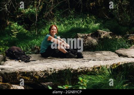 Smiling mid adult woman sitting with dog on footpath in forest Stock Photo