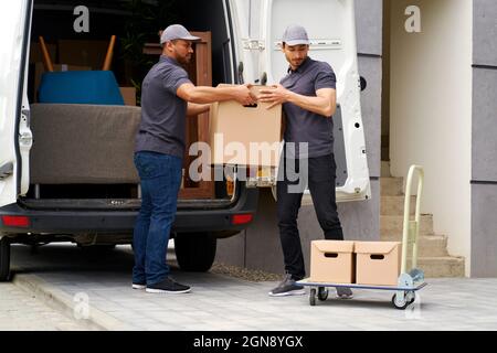 Man helping colleague while unloading boxes from van Stock Photo