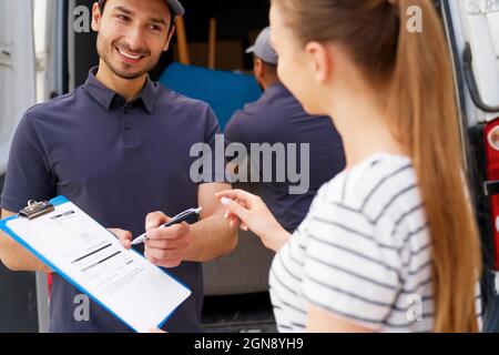 Smiling delivery man looking at female customer while passing pen to sign documents Stock Photo