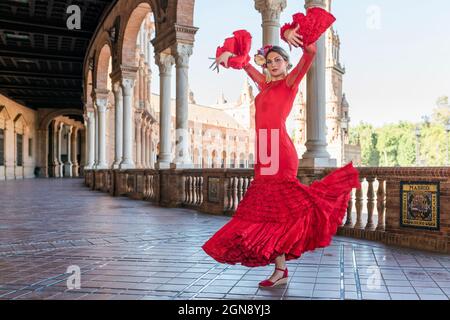 Female flamenco artist dancing with hands raised on walkway at Plaza De Espana, Seville, Spain