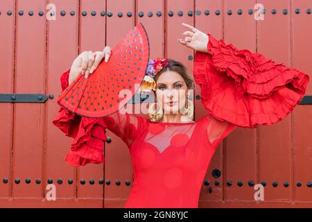 Female flamenco dancer with hand fan dancing in front of red door Stock Photo
