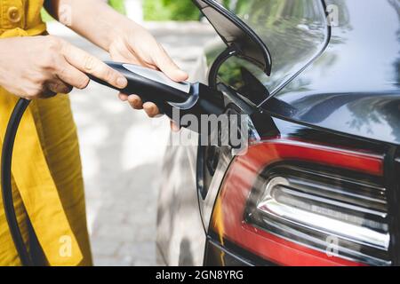 Mature woman holding cable by plug of electric car Stock Photo