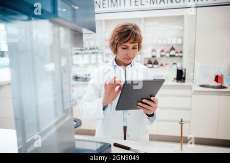 Female pharmacist using digital tablet while standing at laboratory Stock Photo