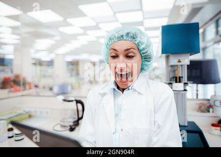 Surprised female pharmacist using digital tablet while standing at laboratory Stock Photo