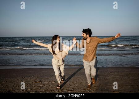 Cheerful couple holding hands while running on beach Stock Photo