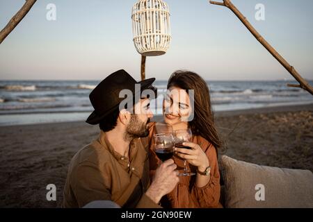 Smiling couple holding drinks while sitting at beach Stock Photo