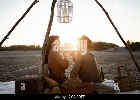 Couple drinking wine while sitting at beach during sunset Stock Photo
