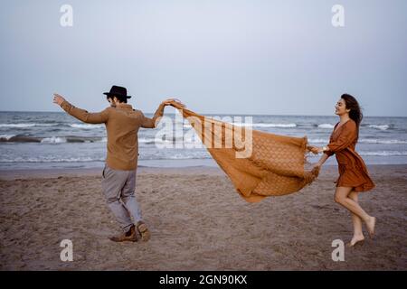 Couple holding blanket while running on beach during sunset Stock Photo