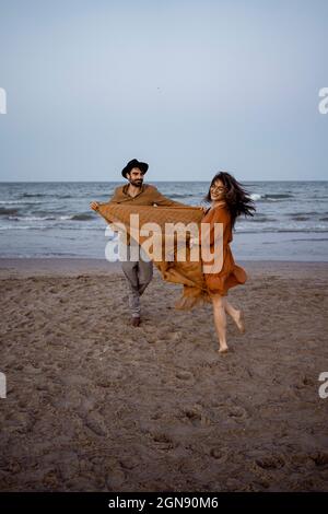 Cheerful couple holding blanket while playing on beach Stock Photo