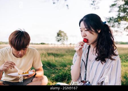 Woman eating strawberry while sitting with man at park during picnic Stock Photo