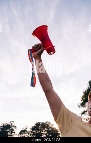 Man with hand raised holding megaphone at park Stock Photo