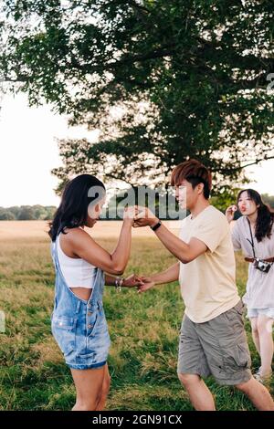 Friends dancing together on meadow with woman standing in background Stock Photo