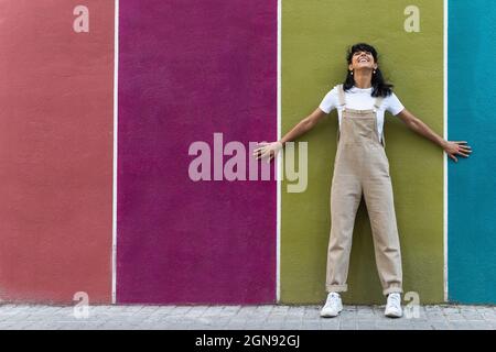Smiling young woman leaning on multi colored wall Stock Photo