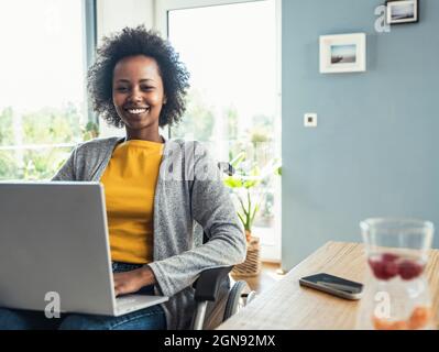 Young female professional using laptop on wheelchair at home Stock Photo