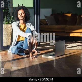 Young woman with eyes closed sunbathing in living room Stock Photo