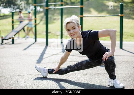 Mature woman with short hair stretching legs at park Stock Photo