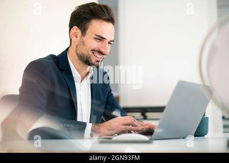 Happy young businessman using laptop while sitting at desk in office Stock Photo