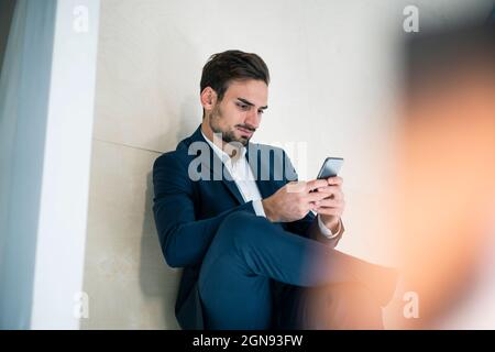 Young businessman text messaging through smart phone while sitting in office Stock Photo