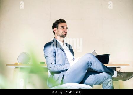 Thoughtful young male professional sitting with digital tablet on chair in office Stock Photo