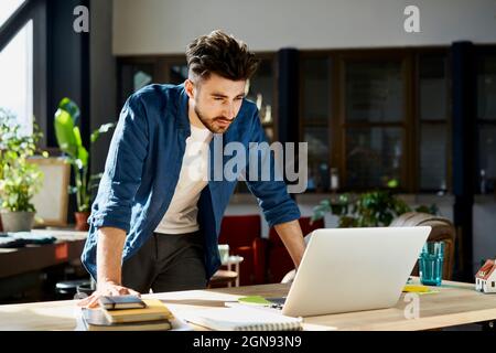 Young businessman looking at laptop in office Stock Photo