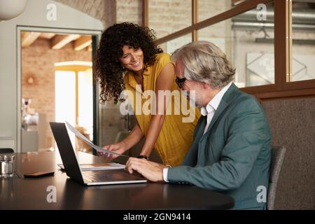 Smiling businesswoman discussing over document with male professional in office Stock Photo