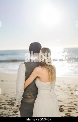 Bride embracing groom on beach during sunrise Stock Photo