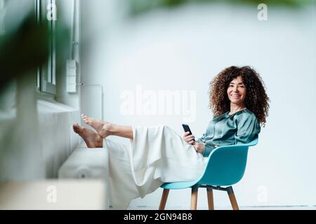 Thoughtful businesswoman with smart phone sitting on chair in office Stock Photo