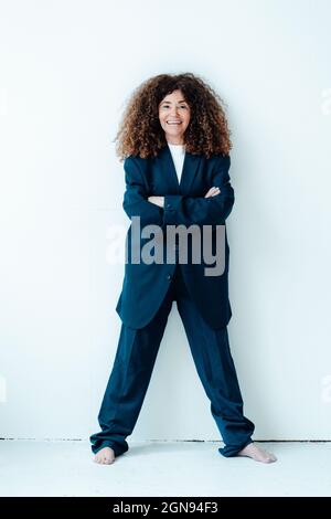 Happy mature businesswoman wearing oversized suit while standing in front of wall Stock Photo