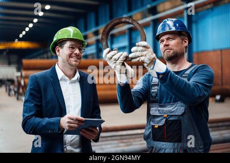 Smiling male manager standing with warehouse worker in factory Stock Photo