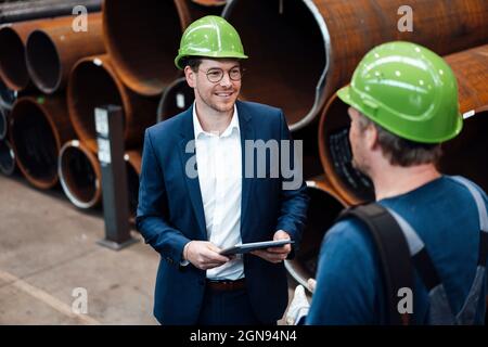 Male manager using laptop while standing by warehouse worker in factory Stock Photo