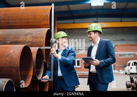Male professional measuring pipe with caliper while standing by coworker at warehouse Stock Photo