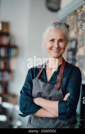 Female cafe owner holding digital tablet while standing in cafe seen through glass window Stock Photo