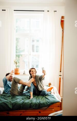 Happy couple taking selfie while sitting on bed at home Stock Photo