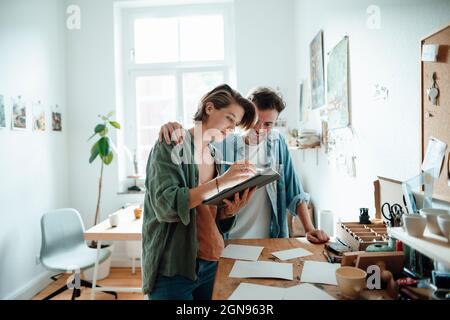 Smiling female illustrator holding spiral notebook and cup on table at home office Stock Photo