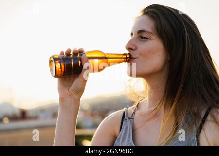 Woman drinking beer at rooftop during sunset Stock Photo