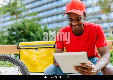 Smiling delivery man using digital tablet on bench Stock Photo