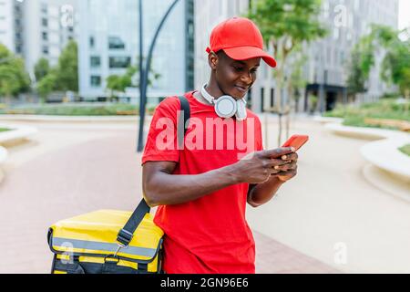 Delivery man wearing backpack text messaging through mobile phone Stock Photo