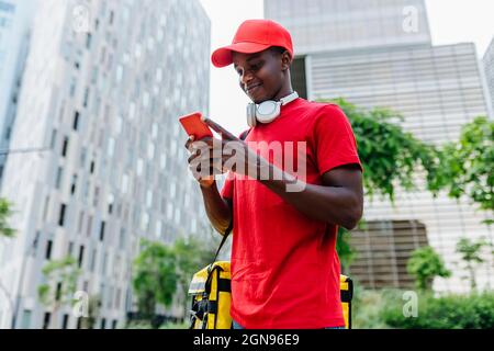 Smiling delivery man text messaging through smart phone in city Stock Photo