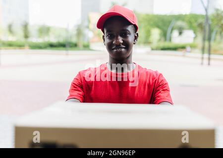 Smiling young delivery man wearing cap delivering package Stock Photo