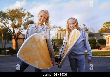 Smiling blond girls with surfboards standing on road Stock Photo