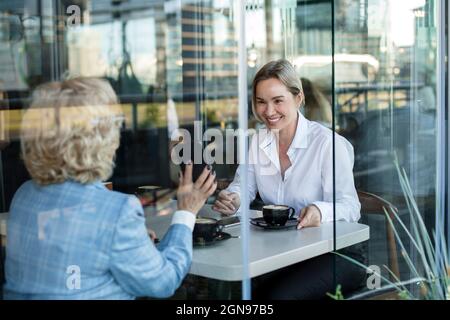Businesswomen discussing while sitting in cafe seen through glass window Stock Photo