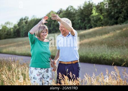Happy senior couple with hands raised dancing while standing at meadow Stock Photo